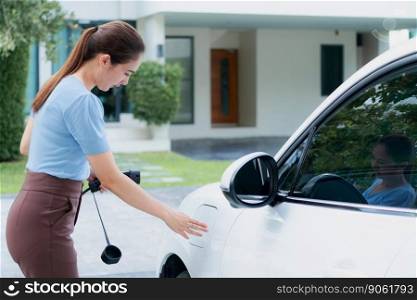 Progressive woman install cable plug to her electric car with home charging station. Concept of the use of electric vehicles in a progressive lifestyle contributes to clean environment.. Progressive woman recharge her EV car at home charging station.