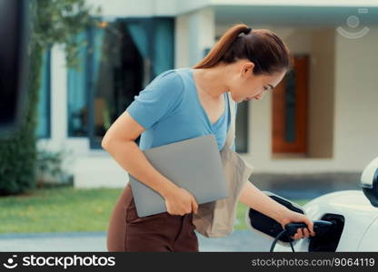 Progressive woman install cable plug to her electric car with home charging station. Concept of the use of electric vehicles in a progressive lifestyle contributes to clean environment.. Progressive woman recharge her EV car at home charging station.