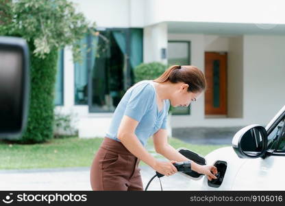 Progressive woman install cable plug to her electric car with home charging station. Concept of the use of electric vehicles in a progressive lifestyle contributes to clean environment.. Progressive woman recharge her EV car at home charging station.