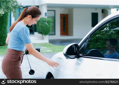 Progressive woman install cable plug to her electric car with home charging station. Concept of the use of electric vehicles in a progressive lifestyle contributes to clean environment.. Progressive woman recharge her EV car at home charging station.