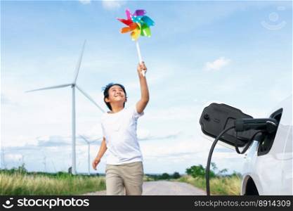 Progressive young asian boy playing with wind pinwheel toy in the wind turbine farm, green field over the hill. Green energy from renewable electric wind generator. Windmill in the countryside concept. Progressive young asian boy playing with wind pinwheel toy at wind turbine farm.