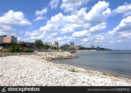 Promenade on the shore of lake Ontario with stones in front and a beautiful blue sky and white clouds in Burlington Ontario.