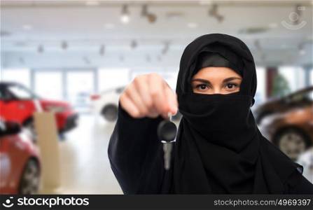 property and people concept - muslim woman in hijab with car key over car show background. muslim woman in hijab with car key over car show