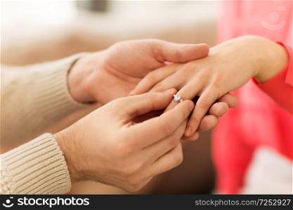 proposal, engagement and relationships concept - close up of man putting diamond ring to female hand at home. man giving diamond ring to woman on valentines day
