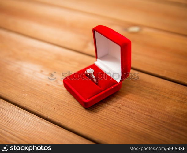 proposal, engagement, valentines day and holidays concept - close up of red gift box with diamond engagement ring on wood