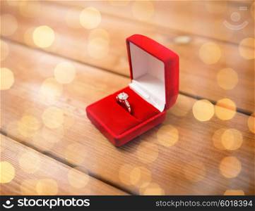 proposal, engagement, valentines day and holidays concept - close up of red gift box with diamond engagement ring on wood