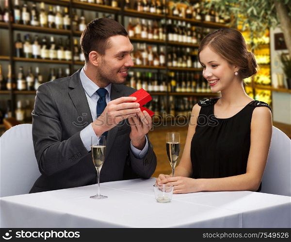 proposal, holiday and luxury concept - happy couple with gift box over restaurant or wine bar background. happy couple with gift box at restaurant
