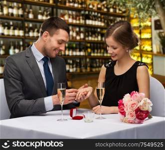 proposal, holiday and luxury concept - smiling man giving engagement ring to woman over restaurant or wine bar background. man proposing to his girlfriend at restaurant