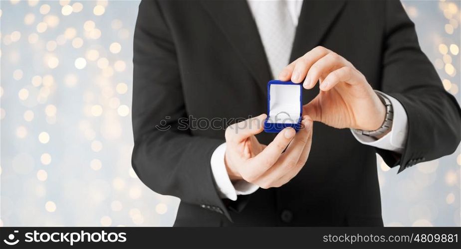 proposal, holidays, jewelry and people concept - close up of man with engagement ring in gift box over lights background