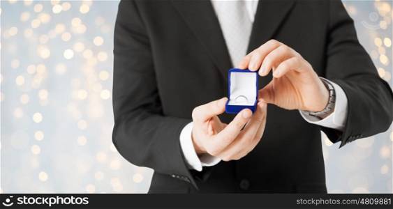 proposal, holidays, jewelry and people concept - close up of man with engagement ring in gift box over lights background
