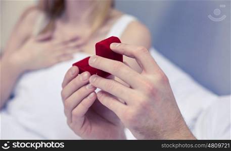 proposal, people, love, holidays and happiness concept - close up of hands holding little red gift box with engagement ring
