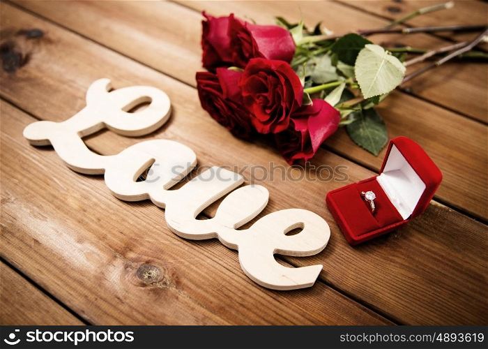 proposal, romance, valentines day and holidays concept - close up of gift box with diamond engagement ring, red roses and word love on wood (vintage effect)