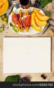 Prosciutto ham with cantaloupe melon, basil leaves and wine over grunge background. Top view, copy space