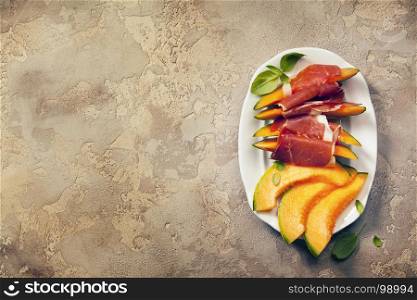 Prosciutto ham with cantaloupe melon, basil leaves and wine over grunge background. Top view, copy space
