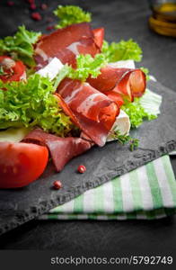 Prosciutto salad with cheese and tomatoes on a plate of natural slate