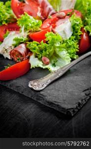 Prosciutto salad with cheese and tomatoes on a plate of natural slate