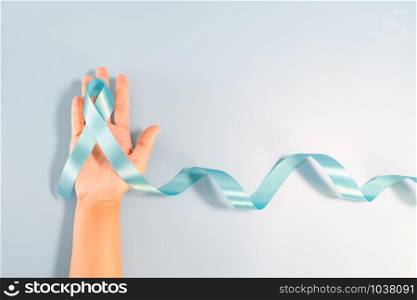 Prostate cancer awareness campaign concept, Men&rsquo;s health concept. hand holding light blue ribbon long tail on blue background. Symbol for support men who living with cancer