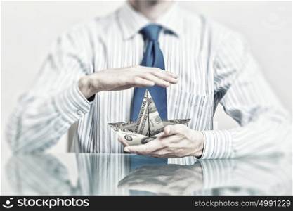 Protect your investments. Hands of businessman holding with care dollar banknote ship