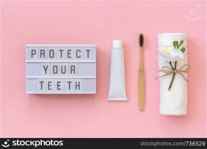Protect your teeth text on light box and natural eco-friendly bamboo brush for teeth, towel, toothpaste tube. Set for washing on pink background. Concept dental health care Top view.. Protect your teeth text on light box and natural eco-friendly bamboo brush for teeth, towel, toothpaste tube. Set for washing on pink background. Concept dental health care Top view