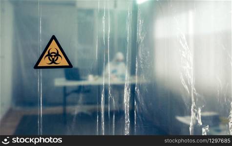 Protective curtain with biohazard symbol through which a scientist is seen working