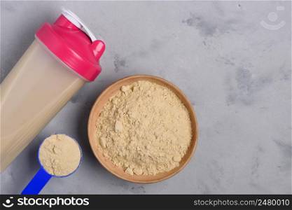 Protein powder in shaker and bowl on concrete background top view