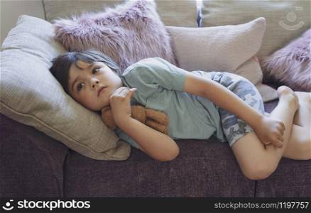 Protrait of happy boy lying on fluffy pillow on sofa, Selective focus Adorable child watching TV and relaxing at home on weekend, Warm and cozy scene in Pastel tone