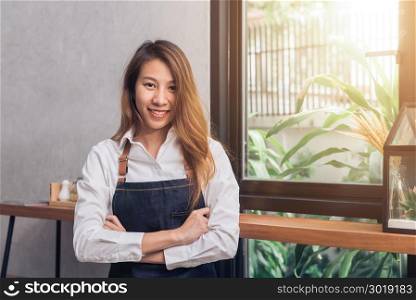 Protrait of young Asian female barista welcome her customer to coffee shop in warm light afternoon with a beautiful smile. Young female barista smile in her small coffee shop. Food and drink concept.