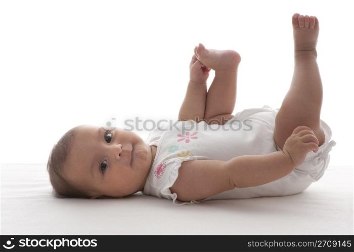 Proud baby girl holding one foot lying on her back on the floor