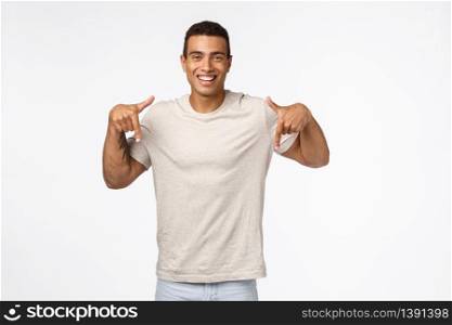Proud, good-looking hispanic male athlete in casual white t-shirt, pointing down and look camera with pleased, happy smile, give advice, promote new product or application, standing satisfied studio.. Proud, good-looking hispanic male athlete in casual white t-shirt, pointing down and look camera with pleased, happy smile, give advice, promote new product or application, standing satisfied studio