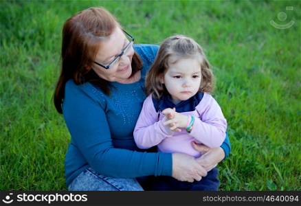 Proud grandmother with her granddaughter sitting on the grass in the field