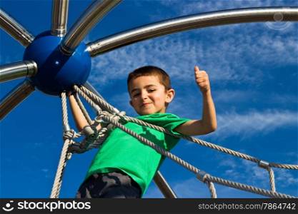 Proud little boy climbs the jungle gym at the park