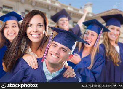 Proud Male Graduate In Cap and Gown with Girl Among Other Graduates Behind.