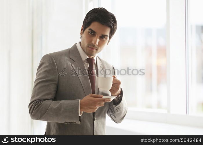 Proud young businesswoman having cup of coffee at office