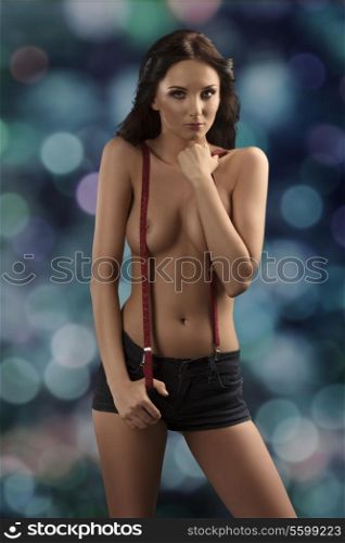 provocative girl posing with naked breast in glamour shoot with long brown hair, red suspenders and sexy shorts
