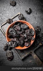Prunes in a plate on a cutting board. On a black background. High quality photo. Prunes in a plate on a cutting board.