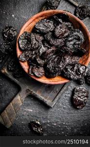 Prunes in a plate on a cutting board. On a black background. High quality photo. Prunes in a plate on a cutting board. 