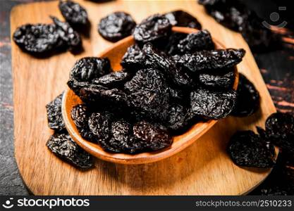 Prunes in a plate on a wooden cutting board. Against a dark background. High quality photo. Prunes in a plate on a wooden cutting board.