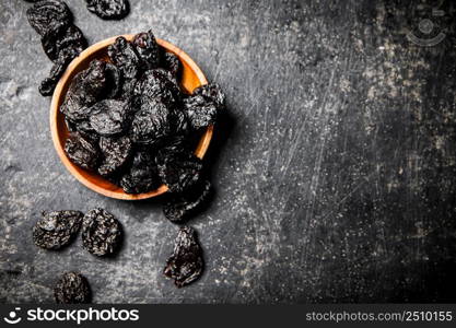 Prunes in a wooden plate on the table. On a black background. High quality photo. Prunes in a wooden plate on the table.