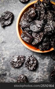 Prunes in a wooden plate on the table. On a black background. High quality photo. Prunes in a wooden plate on the table. 