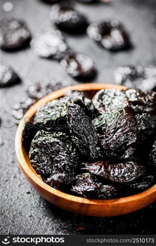 Prunes in a wooden plate on the table. On a black background. High quality photo. Prunes in a wooden plate on the table.