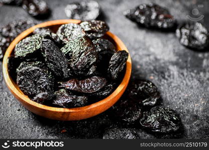 Prunes in a wooden plate on the table. On a black background. High quality photo. Prunes in a wooden plate on the table.