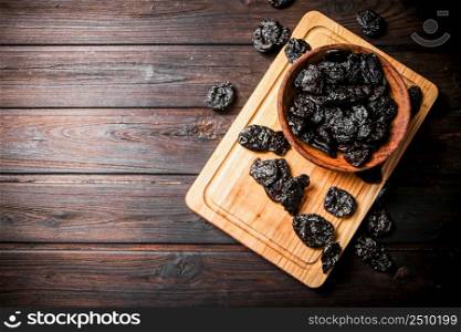 Prunes on a wooden cutting board. On a dark wooden background. High quality photo. Prunes on a wooden cutting board.