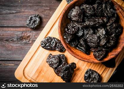 Prunes on a wooden cutting board. On a dark wooden background. High quality photo. Prunes on a wooden cutting board.