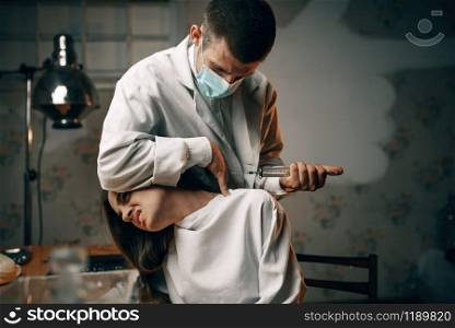 Psychiatrist with syringe makes a sedative injection to crazy female patient, mental hospital. Woman undergoing treatment in clinic for the mentally ill. Psychiatrist with syringe makes sedative injection