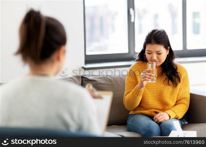psychology and mental therapy concept - young asian woman patient drinking water and psychologist at psychotherapy session. young asian woman patient and psychologist