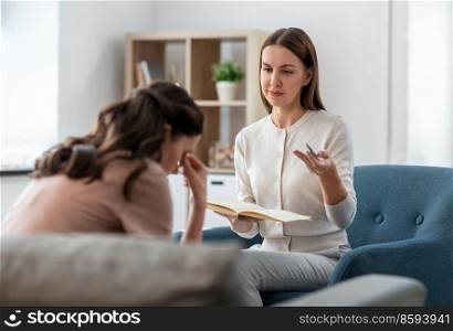 psychology, mental health and people concept - psychologist with notebook talking to stressed woman patient at psychotherapy session. psychologist and woman at psychotherapy session