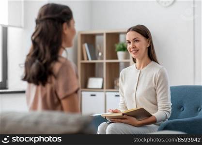psychology, mental health and people concept - smiling psychologist with notebook and woman patient at psychotherapy session. psychologist and woman at psychotherapy session