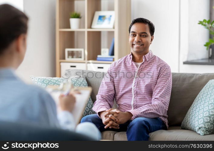 psychology, mental therapy and people concept - happy smiling young indian man patient and woman psychologist at psychotherapy session. man and psychologist at psychotherapy session