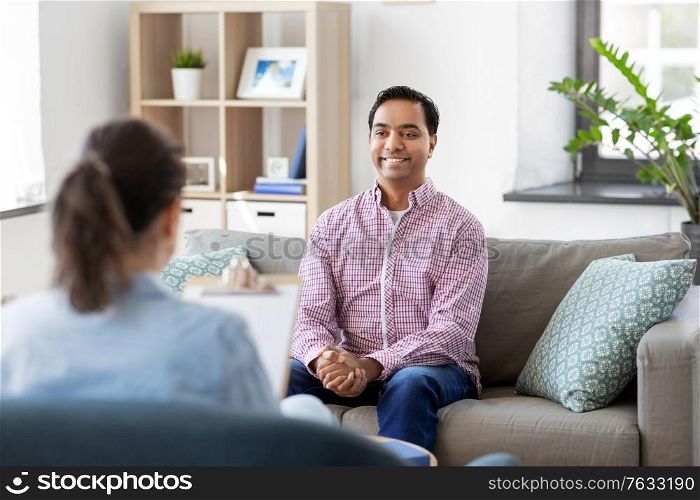psychology, mental therapy and people concept - happy smiling young indian man patient and woman psychologist at psychotherapy session. man and psychologist at psychotherapy session