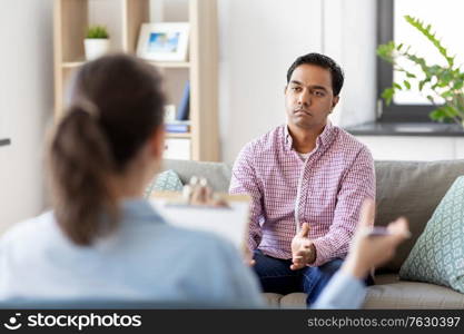 psychology, mental therapy and people concept - sad young indian man patient and woman psychologist at psychotherapy session. man and psychologist at psychotherapy session